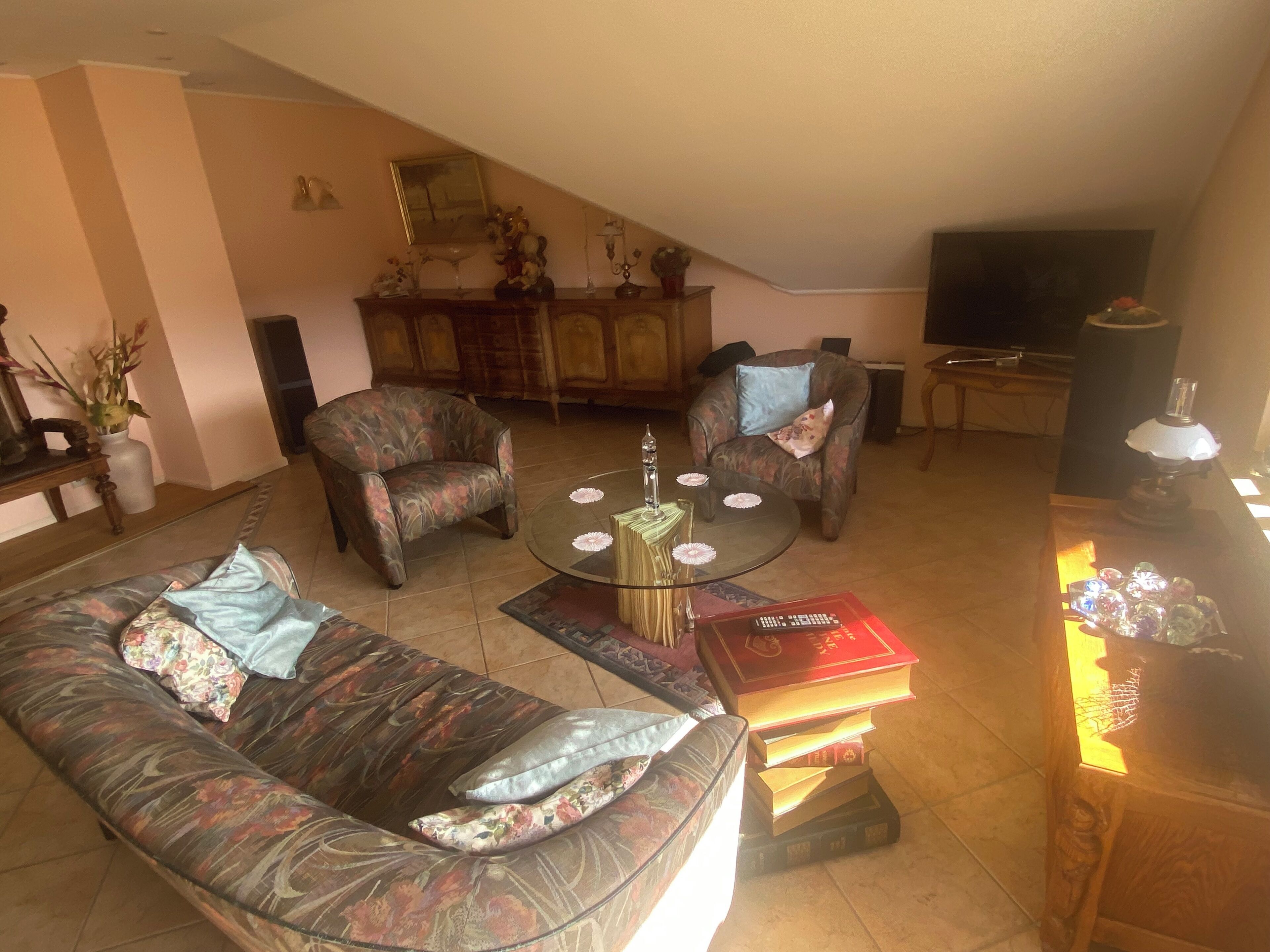 Un salon comprenant un canapé, deux fauteuils, une table basse, un téléviseur et un meuble contenant des objets décoratifs.