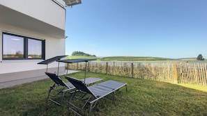 Un edificio moderno con un patio que cuenta con dos tumbonas y una mesa, con vistas a un campo vallado.