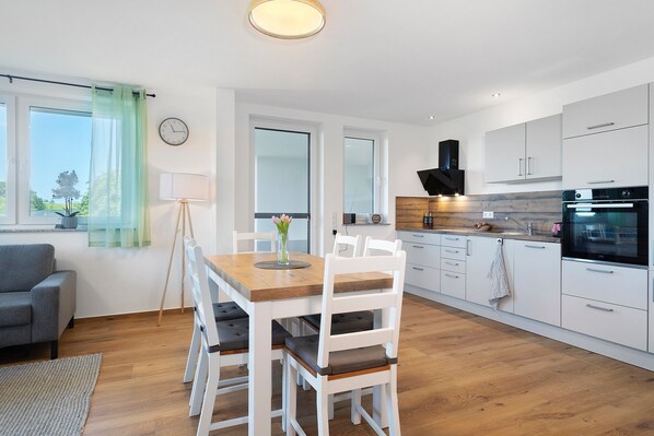 Una cocina moderna con armarios blancos, una mesa de comedor de madera y un sofá gris.