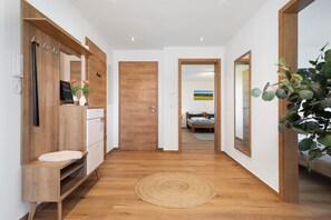 Un pasillo con suelo de madera, un tapete redondo tejido, una puerta de madera y un espejo que refleja una habitación con una cama y un cuadro.