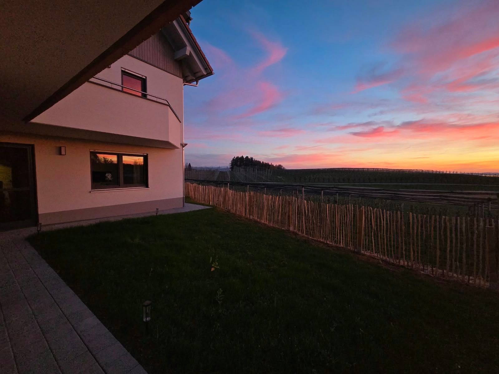 A modern house with a flat roof and a balcony overlooking a field.