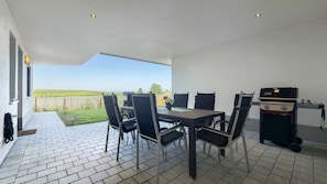 Eine Terrasse im Freien mit Tisch und Stühlen, einem Grill und Blick auf die Landschaft.