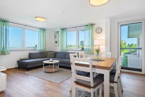Una sala moderna con un sofá, una mesa de comedor, sillas y ventanas grandes.