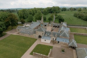 A large stone building with multiple wings and a central tower, surrounded by green fields and trees. - The Dairy at Rosebery Steading, Gorebridge (Temple)