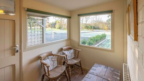 Une pièce d’angle avec deux chaises en bois, une petite table et deux fenêtres aux cadres verts.