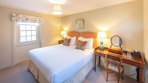 Un lit bien fait, avec du linge de lit blanc, deux lampes de chevet, un bureau en bois avec un miroir et une petite chaise.