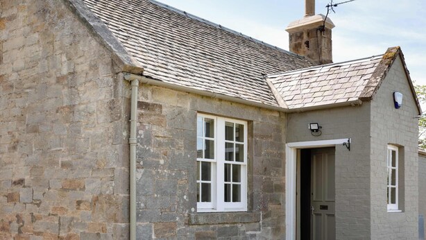 Un bâtiment en pierre doté d’un toit à deux versants, d’une porte et d’une fenêtre.