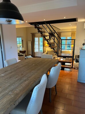 Un espace repas avec une table et des chaises en bois, un escalier et une vue sur l’extérieur.