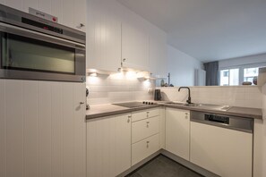 A modern kitchen with white cabinets, a built-in oven, a dishwasher, and a stainless steel sink. - Knokke City Centre Apartment for 6 (KNOKKE-HEIST)