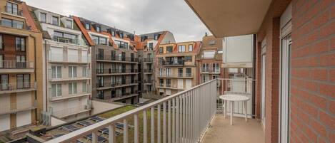 Ein Wohngebäude mit mehreren Balkonen, von denen einige mit Solaranlagen ausgestattet sind, und einer kleinen Außen-Sitzgelegenheit.