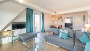 A modern living room with a grey sofa, glass coffee table, and a flat-screen TV mounted on the wall. - 3-Bedroom Sunny Apartment in Knokke (KNOKKE-HEIST)