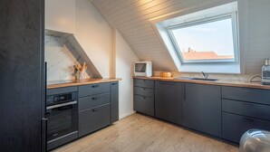 A modern kitchen with dark cabinetry, a built-in oven, a microwave, and a window with a view of the cityscape. - 3-Bedroom Sunny Apartment in Knokke (KNOKKE-HEIST)