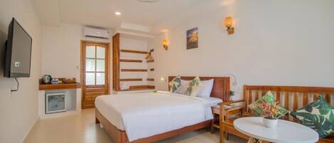 A hotel room with a bed, bedside table, chair, small table, and a TV.