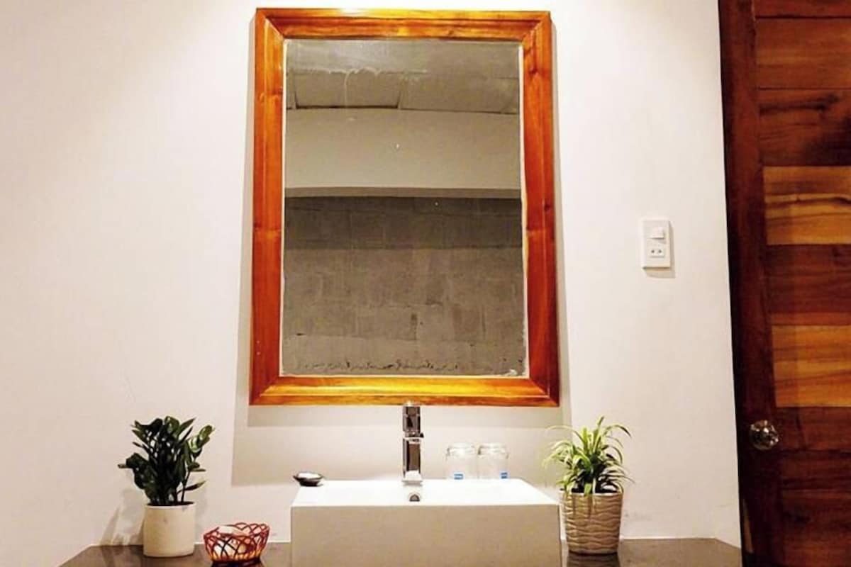 A bathroom with a white sink, a wooden-framed mirror, and two potted plants on the counter.