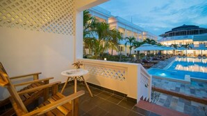 Ein Balkon mit Blick auf einen Pool, Palmen und ein Gebäude mit einer kreisförmigen Struktur.