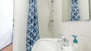 Een badkamer met een witte wastafel, een handdouche en een blauw patroon gordijn.