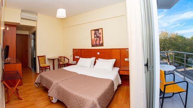 A hotel room with a double bed, a desk with a chair, a small table, and a balcony with a chair. - Hotel Ena - Cozy Mountain View Suite With Pool (Lamia)
