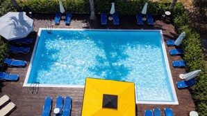 A rectangular swimming pool with clear blue water, surrounded by blue lounge chairs and umbrellas. - Hotel Ena - Cozy Mountain View Suite With Pool (Lamia)