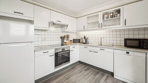 Moderni keittiö, jossa on valkoiset kaapit, sisäänrakennettu uuni, mikroaaltouuni ja astianpesukone.