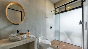 A modern bathroom with a concrete countertop, a round mirror, a toilet, and a glass shower enclosure. - HOTEL NELBLU #4 - DOUBLE BEDS (Playa Flamingo)