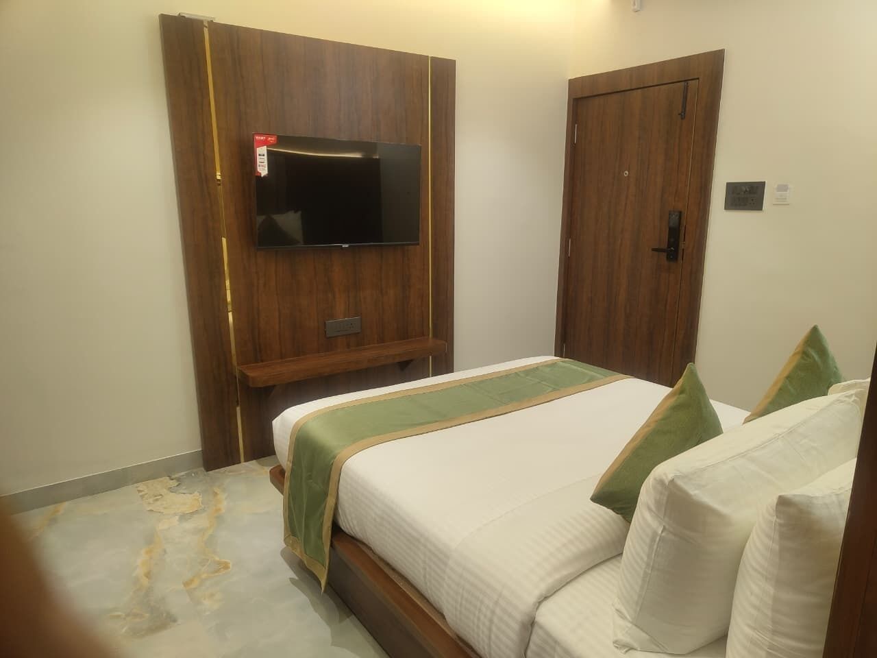 A hotel room with a bed, a TV mounted on a wooden panel, and a door.