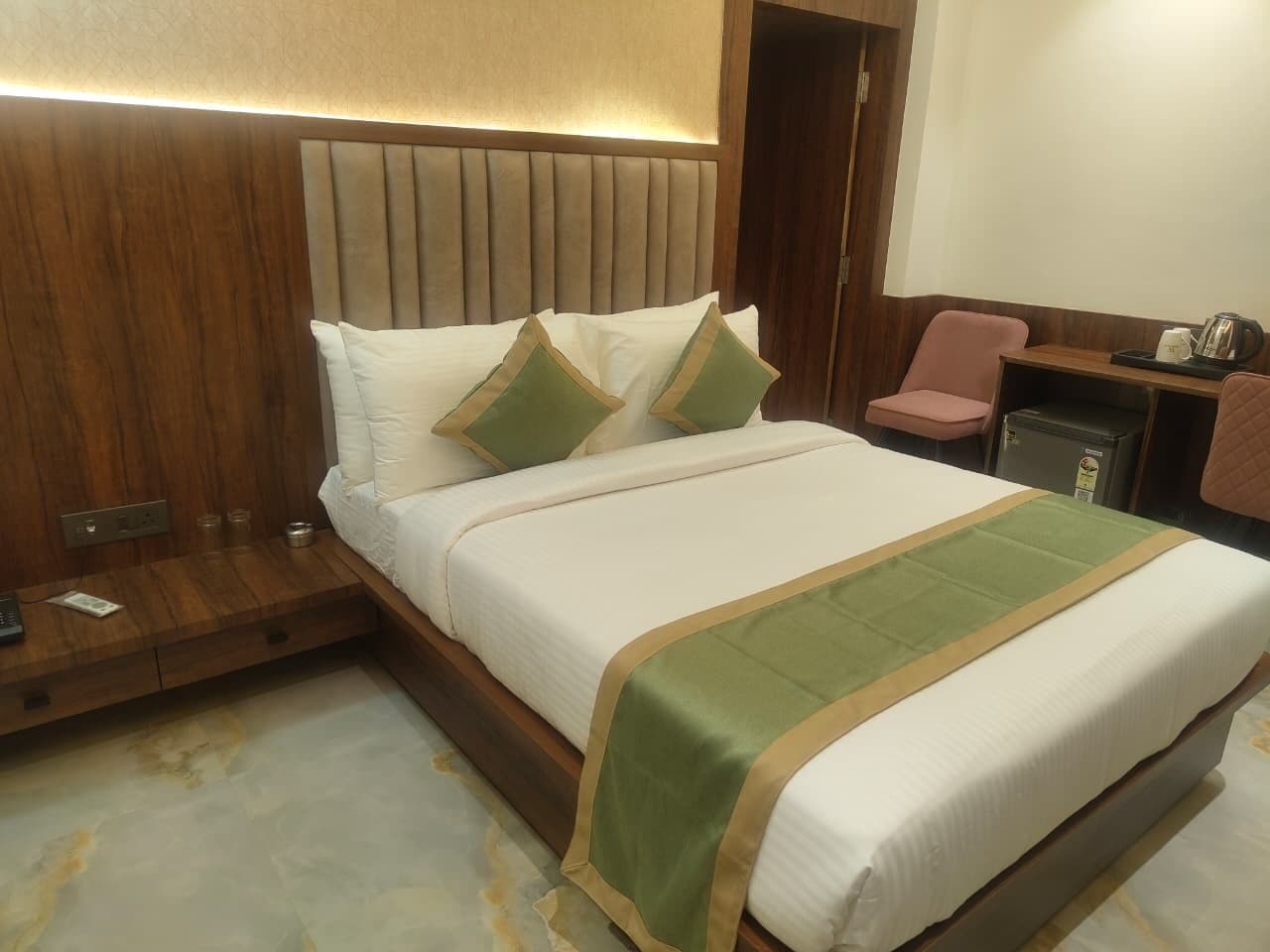 Habitación de hotel con una cama grande, cabecera de madera, mesitas de noche, un escritorio pequeño y una silla.