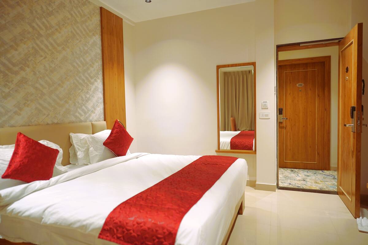 Habitación de hotel con una cama grande, almohadas rojas, una puerta de madera y un espejo.