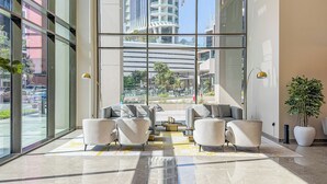Un vestíbulo moderno con amplios ventanales, una zona de estar con sofás y vistas a un paisaje urbano.