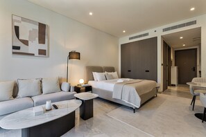 Una habitación de hotel moderna con un sofá, una cama, una mesita y una lámpara.
