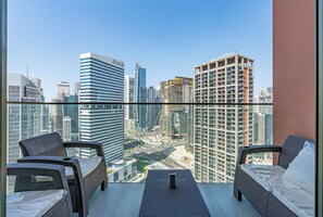A balcony with two wicker chairs and a small table, overlooking a cityscape with modern high-rise buildings. - Elegant Studio with Iconic Burj Khalifa Views (Dubai)