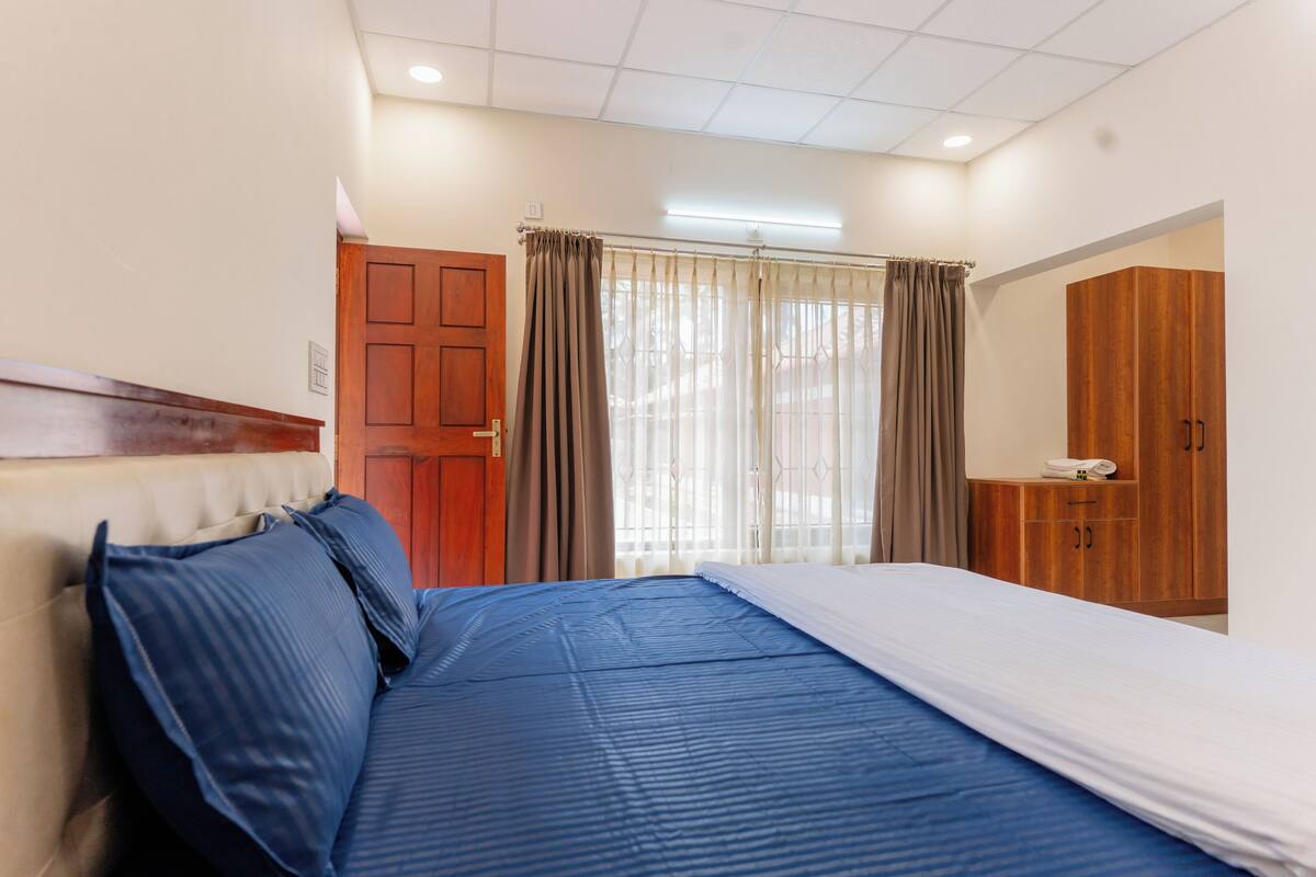 A hotel room with a bed, wooden wardrobe, and a window with curtains.
