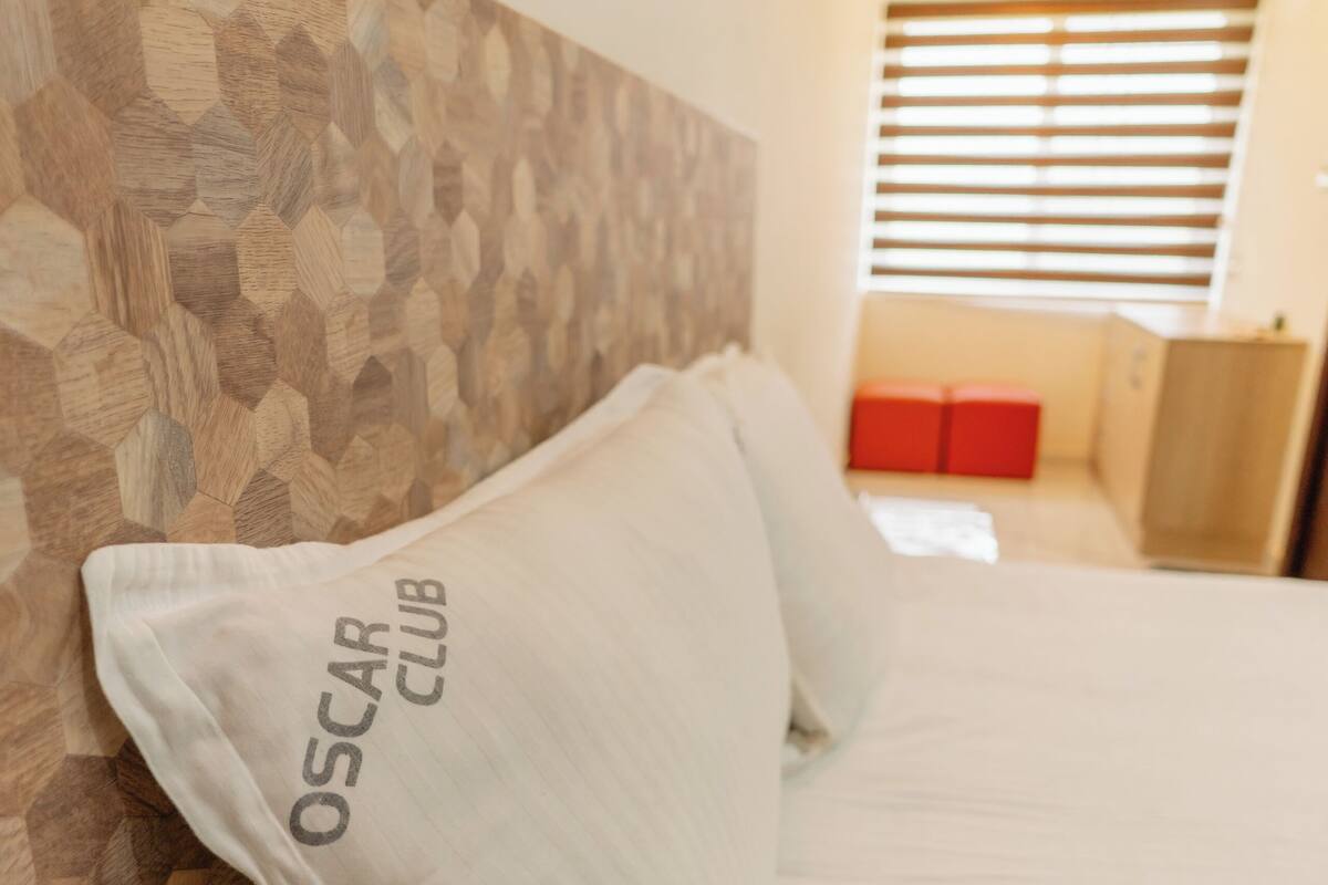 A bed with white bedding and pillows, a wooden headboard, and a red bench in the background.