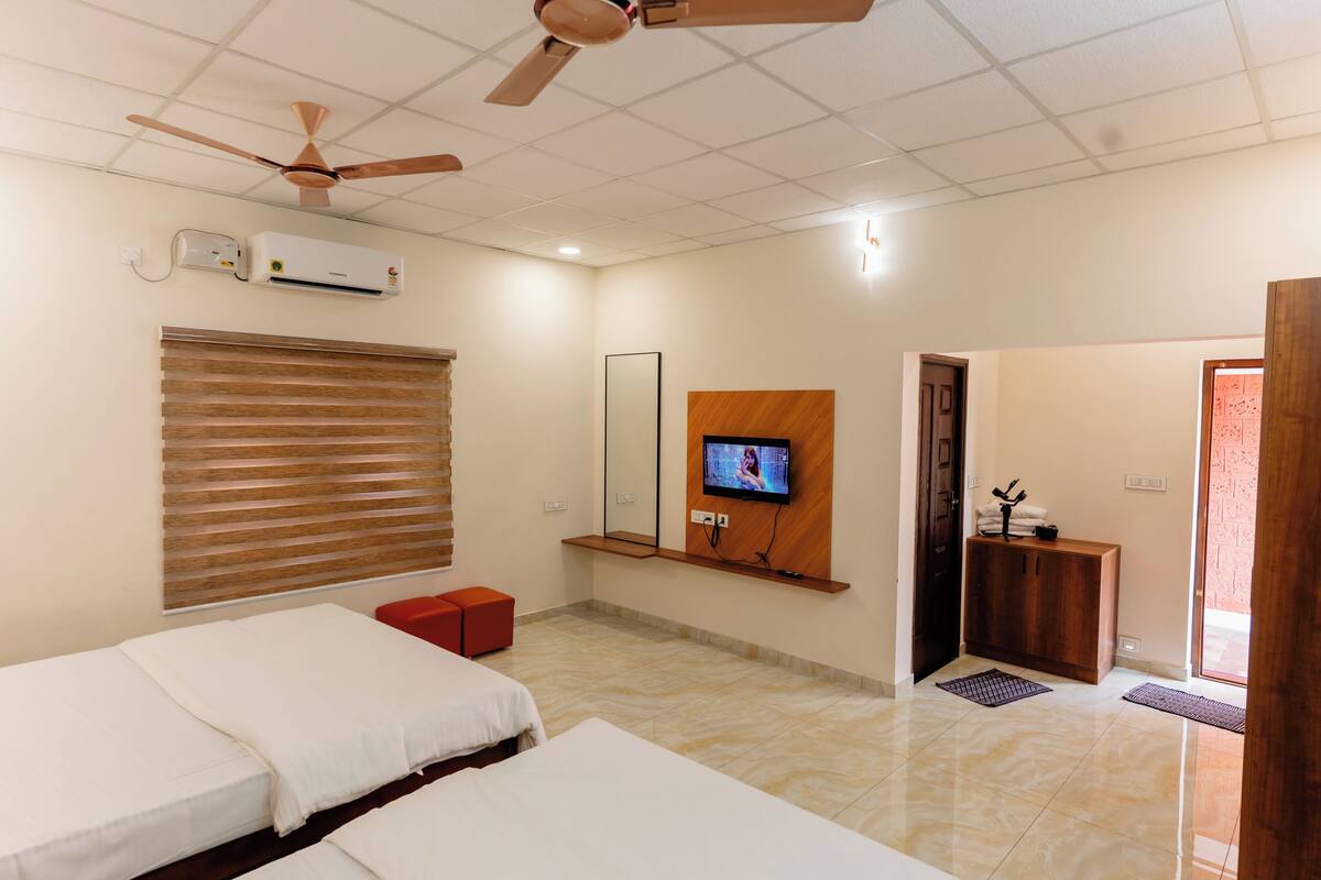 A hotel room with two beds, a TV mounted on the wall, a ceiling fan, and an air conditioning unit.