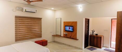 A hotel room with two beds, a TV mounted on the wall, a ceiling fan, and an air conditioning unit.