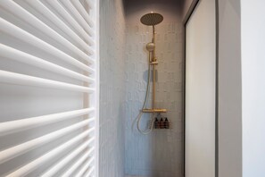 Une douche dotée d’un pommeau de douche doré et d’un panneau de commande fixé au mur.