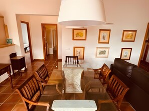 Un comedor con una mesa de vidrio, sillas de madera, un sofá de cuero negro y cuadros en las paredes.
