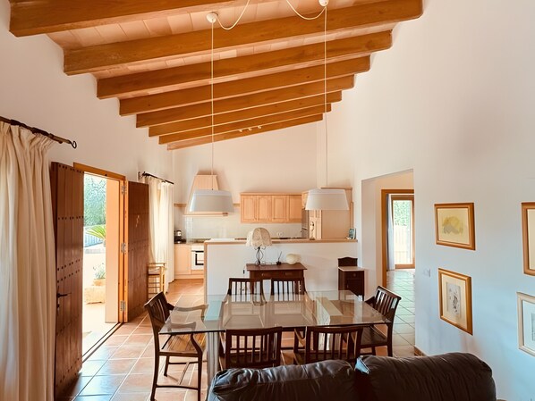 Un comedor amplio con una mesa de vidrio y sillas de madera, una cocina con armarios de madera y un techo con vigas a la vista.