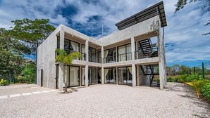 Un immeuble moderne à plusieurs étages, doté d’une façade en béton, de grandes fenêtres et d’une allée gravillonnée.