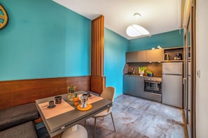 A compact kitchen with a dining area, featuring a wooden bench, a table with a coffee maker, and a modern pendant light. - Alternative Resort & SPA Apartments (Scorrano)