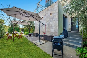 Une terrasse avec des meubles d’extérieur, un barbecue et un mur en pierre.
