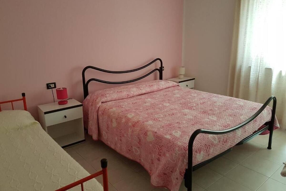 A bedroom with a single bed, a nightstand, a lamp, and a window with curtains.