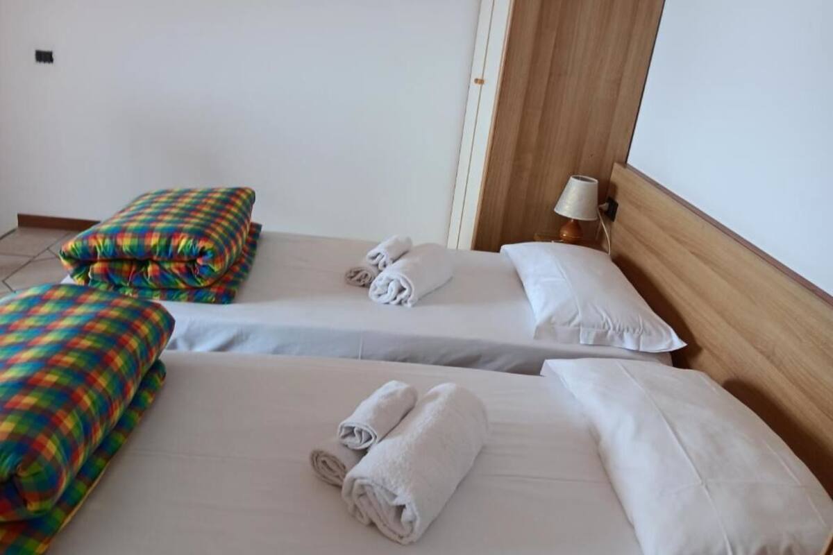 Two single beds with white linens and colorful plaid blankets, a wooden headboard, and a bedside lamp.
