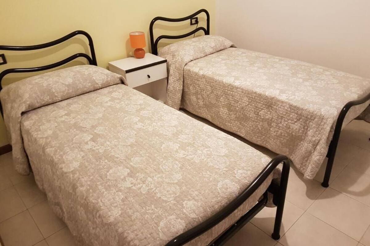 A room with two beds, each with a headboard and a bedside table with a lamp.