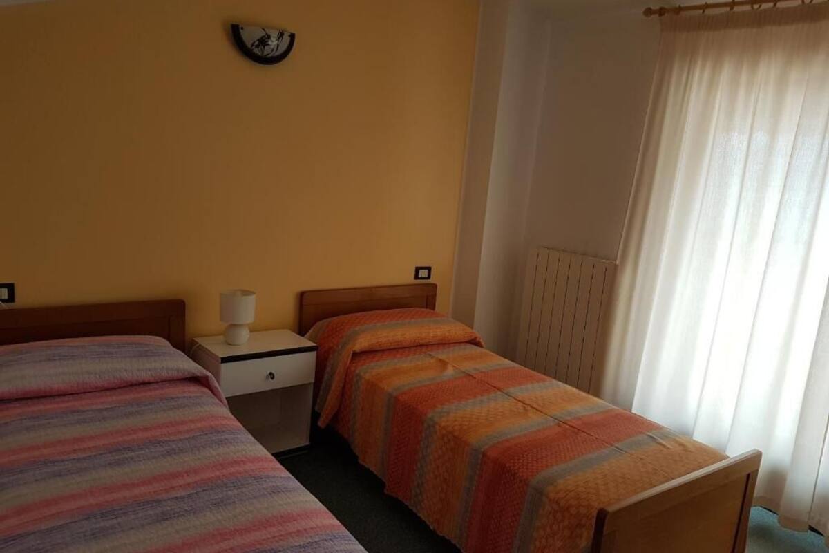 A room with two beds, a nightstand, a lamp, and a window with curtains.