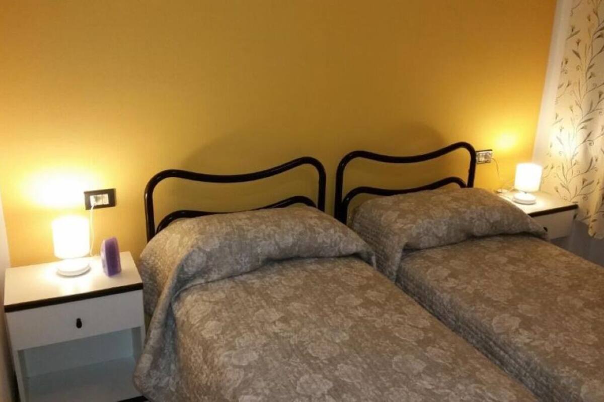 A twin room with two single beds, a bedside table with a lamp, and a curtain with a leaf pattern.