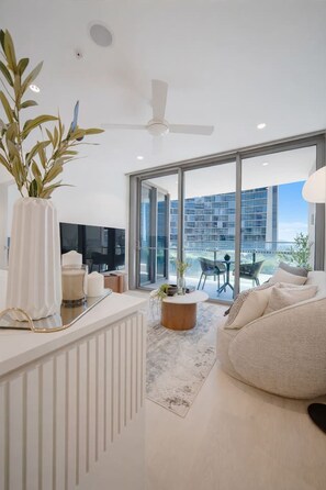 Ein modernes Wohnzimmer mit großem Fenster, Deckenventilator und Blick auf eine Stadtlandschaft.