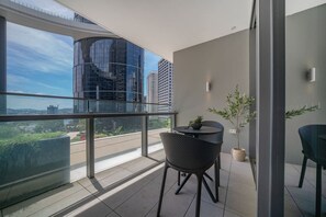 A balcony with a view of a cityscape, a round table with chairs, and a potted plant. - Modern City 1-Bedroom | Prime CBD Location (Brisbane City)