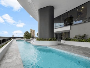 A swimming pool with a modern architectural design, surrounded by a landscaped area with plants. - Modern City 1-Bedroom | Prime CBD Location (Brisbane City)