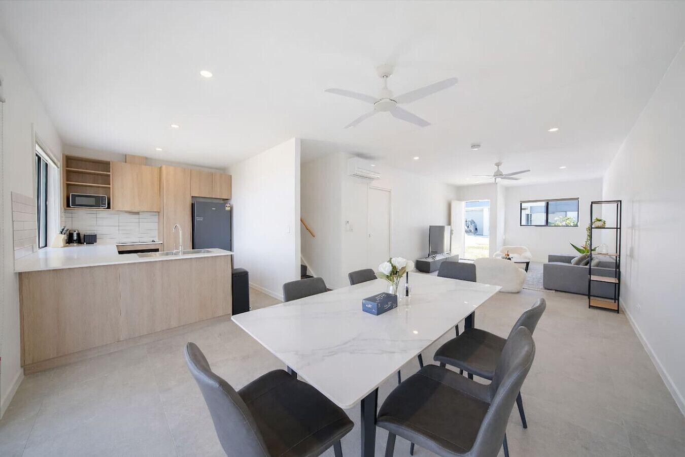 A modern kitchen with a built-in microwave, a refrigerator, and a dining area with a marble table and chairs.
