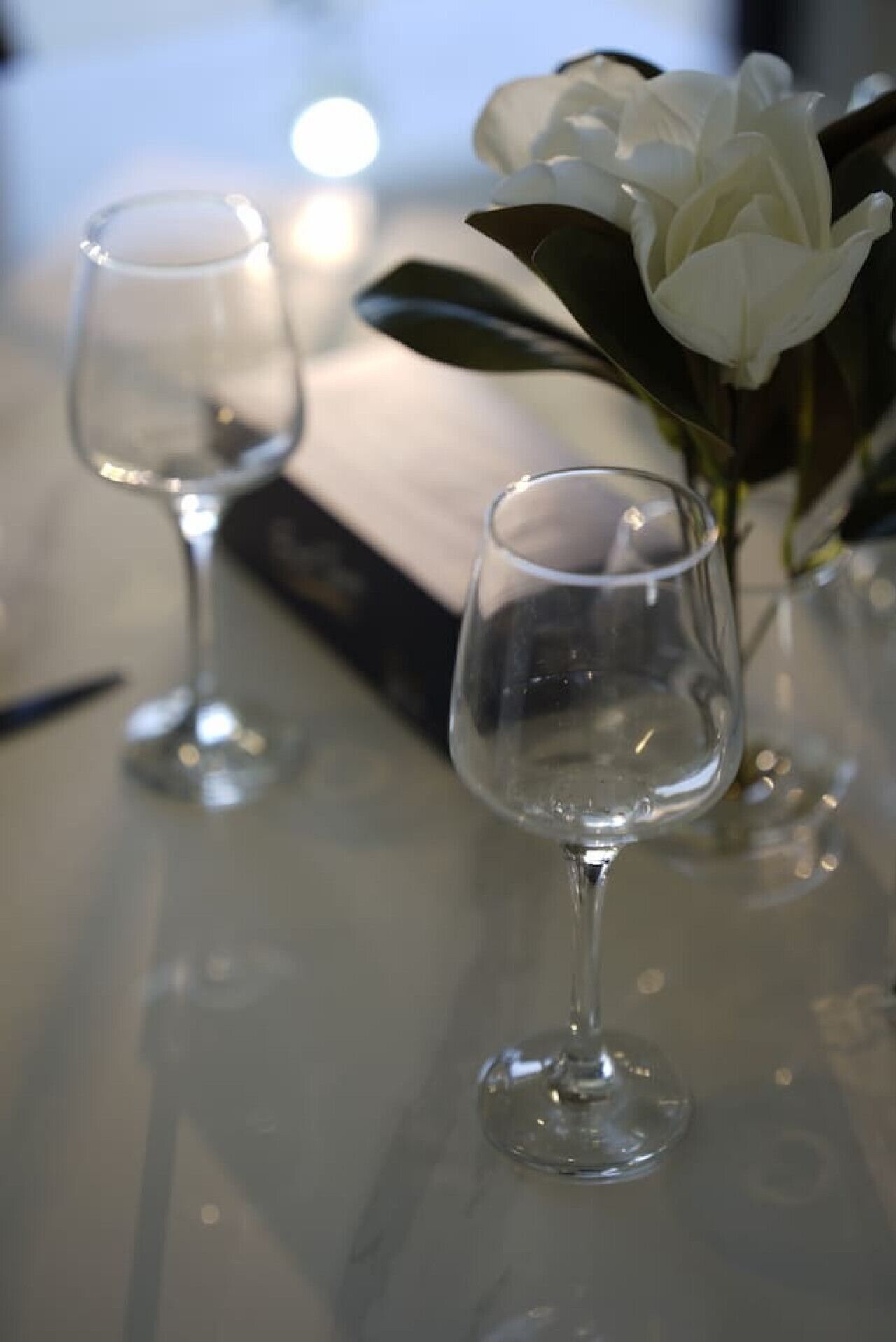 Two empty wine glasses on a table with a white flower in the background.